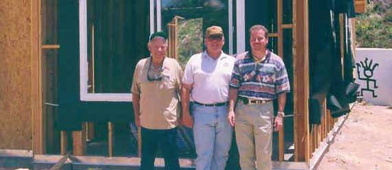 photograph of Tom, his dad and granpa standing on front of a house frame in a construction site.